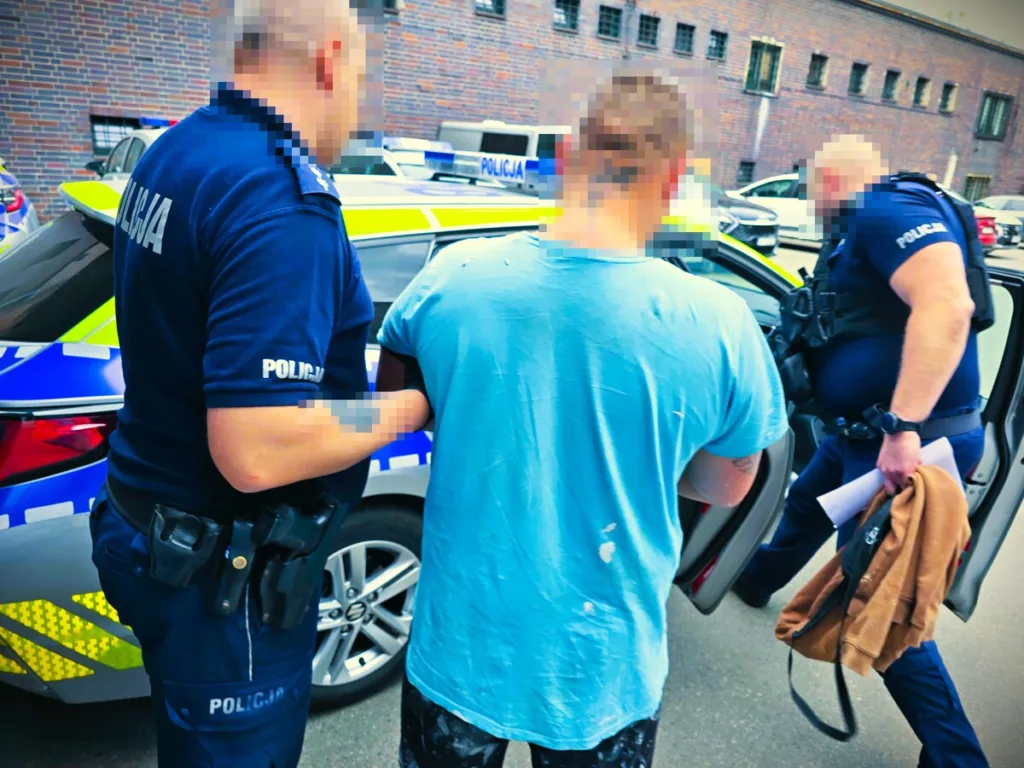 dwóch funkcjonariuszy policji prowadzący zatrzymanego do radiowozu